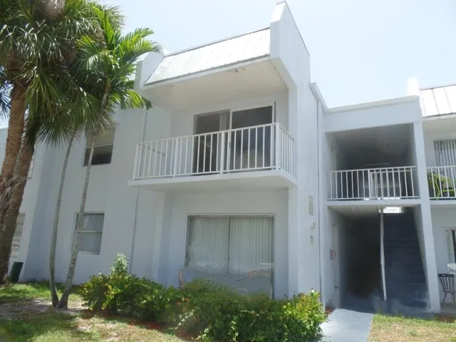 Multi-story stucco exterior featuring a second-floor balcony with white railings, sliding glass doors, and a metal roof