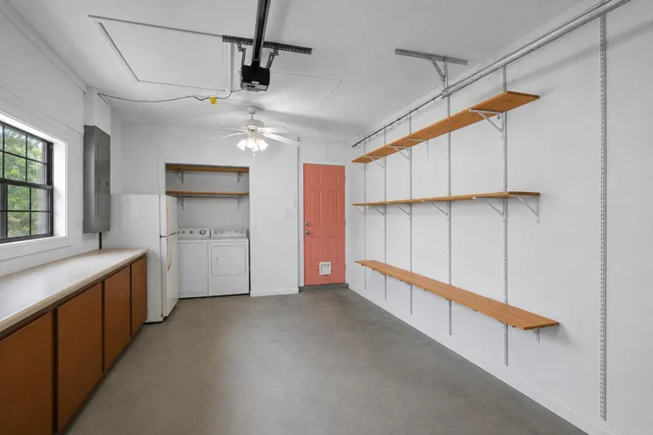 Spacious garage featuring concrete flooring, built-in cabinetry with a countertop, adjustable wall-mounted shelving, and a laundry area