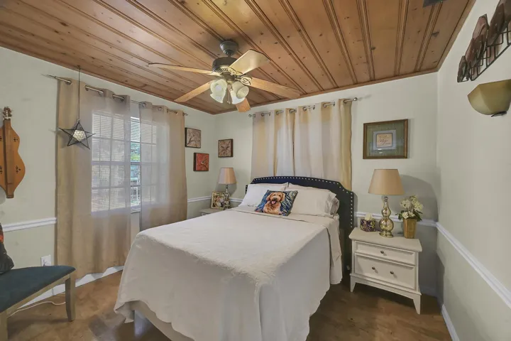 Room featuring a wood-panel ceiling, ceiling fan with light kit, wood-finish flooring, two large windows, and chair rail molding