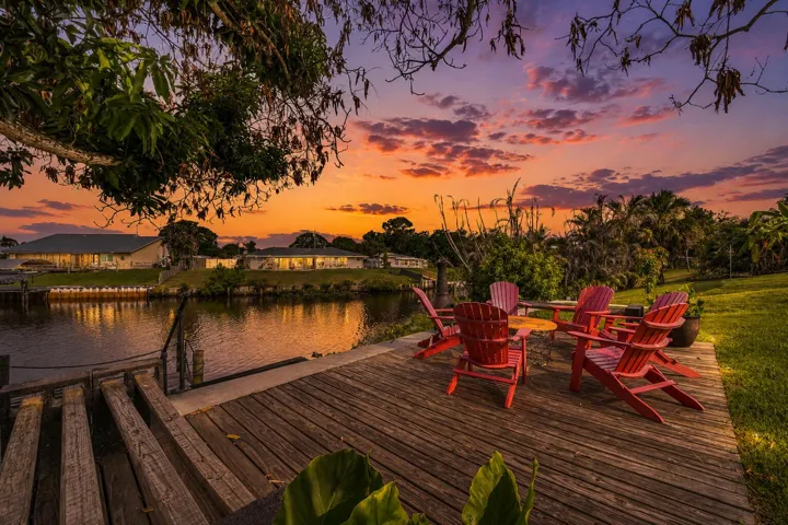 Waterfront property featuring a wooden deck with built-in steps, a grassy area, and lush tropical landscaping