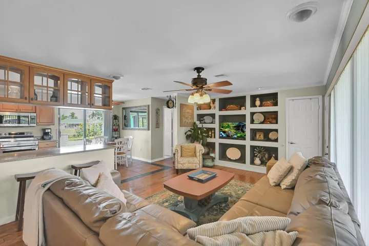 Open-concept living area featuring wood-finish flooring, a built-in shelving unit, and a ceiling fan with light fixture