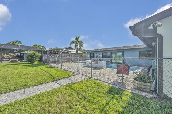 Expansive backyard featuring a manicured lawn, patterned concrete pathway, chain-link fencing, a swimming pool with paved surround, and a screened enclosure