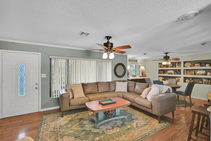 Living area featuring wood-finish flooring, a white paneled entry door with decorative glass inlay, and a large window with vertical blinds