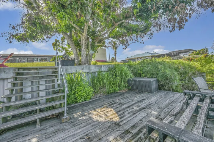 Wood-finish dock area featuring steps with a metal handrail, mature trees, lush greenery, and a concrete retaining wall