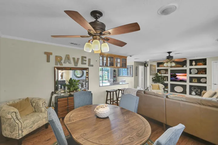 Open-concept living area featuring wood-finish flooring, crown molding, and a ceiling fan with integrated lighting