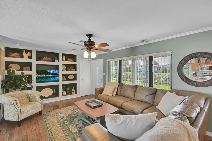 Spacious living area featuring wood-finish flooring, a built-in media center with shelving, and large windows providing abundant natural light