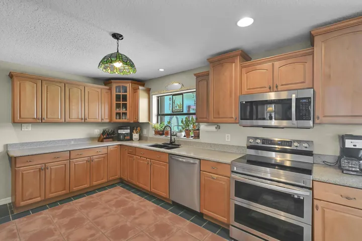 Kitchen featuring light wood-finish cabinetry, light speckled countertops, a stainless steel electric range, and coordinated stainless steel microwave