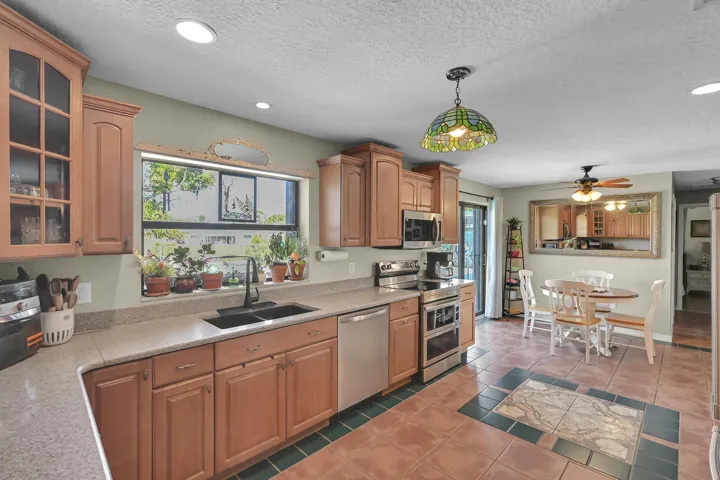 Kitchen featuring wood-finish cabinetry, stainless steel appliances, a black basin sink with a black faucet, and light-toned countertops