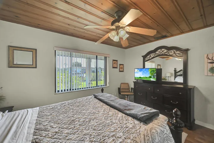 Spacious room featuring a wood-panel ceiling, ceiling fan with light fixture, large window with vertical blinds, and wood-finish flooring