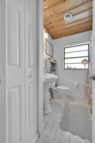 Bathroom featuring a wood-panel ceiling, pedestal sink, and tiled flooring