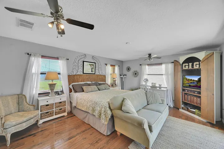 Spacious room featuring wood-finish flooring, light gray walls, and multiple windows with blinds and sheer white curtains