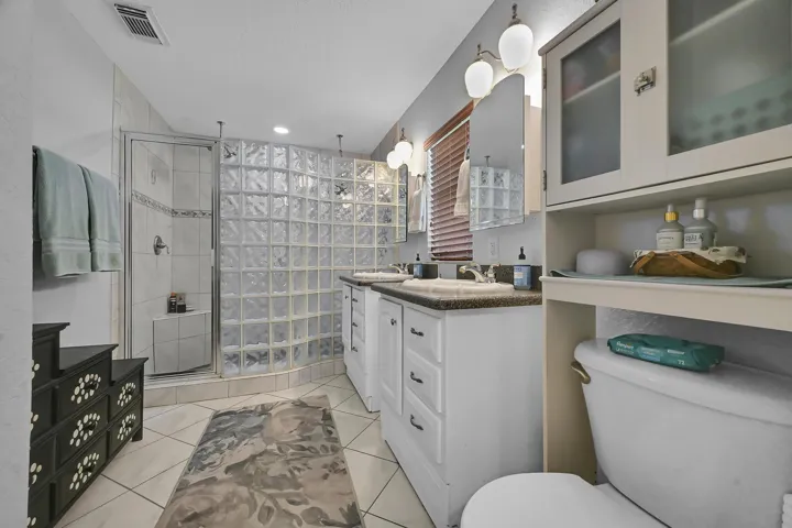 Bathroom featuring a glass block shower enclosure, tiled shower with built-in bench, dual vanity with undermount sinks, and an integrated toilet cabinet with frosted glass doors