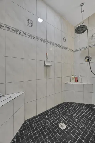 Shower enclosure featuring white tiled walls with decorative accent banding