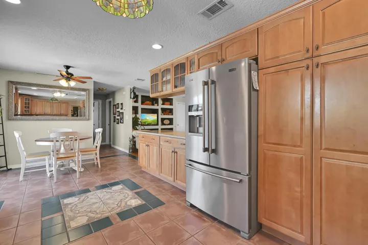 Kitchen area featuring extensive wood cabinetry, a stainless steel refrigerator, and terracotta-style floor tiling with decorative inserts