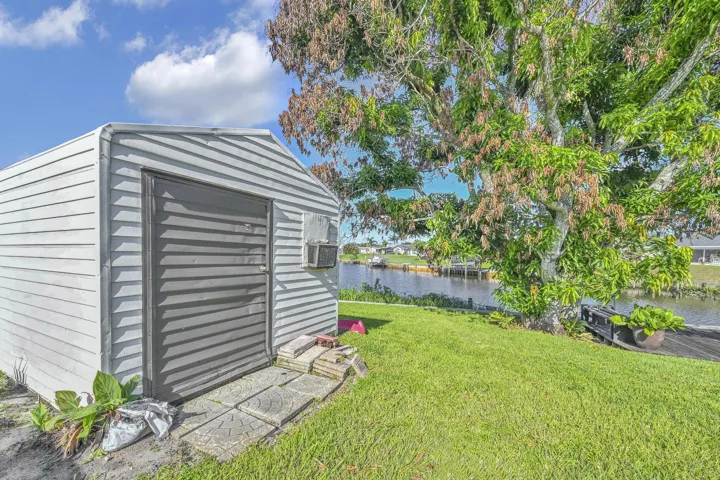 Waterfront property featuring a storage shed with horizontal siding, a substantial mature tree, and a green lawn extending to the water's edge