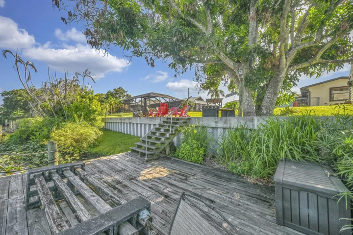 Waterside wood-plank deck featuring a boat lift, steps leading to a raised green lawn, and a large mature tree