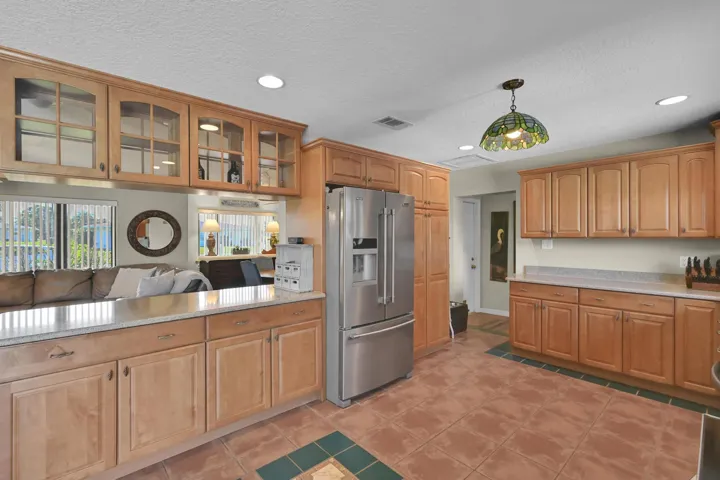 Kitchen featuring wood-finish cabinetry, stainless steel refrigerator, stone countertops, and tile flooring