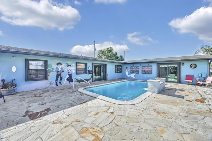 Rear exterior featuring an in-ground swimming pool, flagstone patio, multiple windows, and a sliding glass door