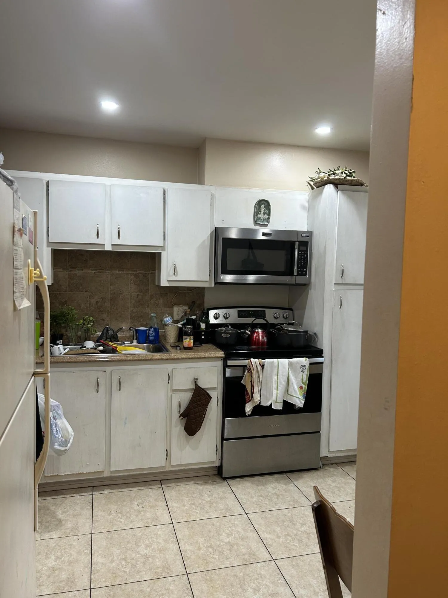 Galley-style kitchen featuring tiled flooring, white cabinetry, and a stainless steel oven/range with an overhead microwave