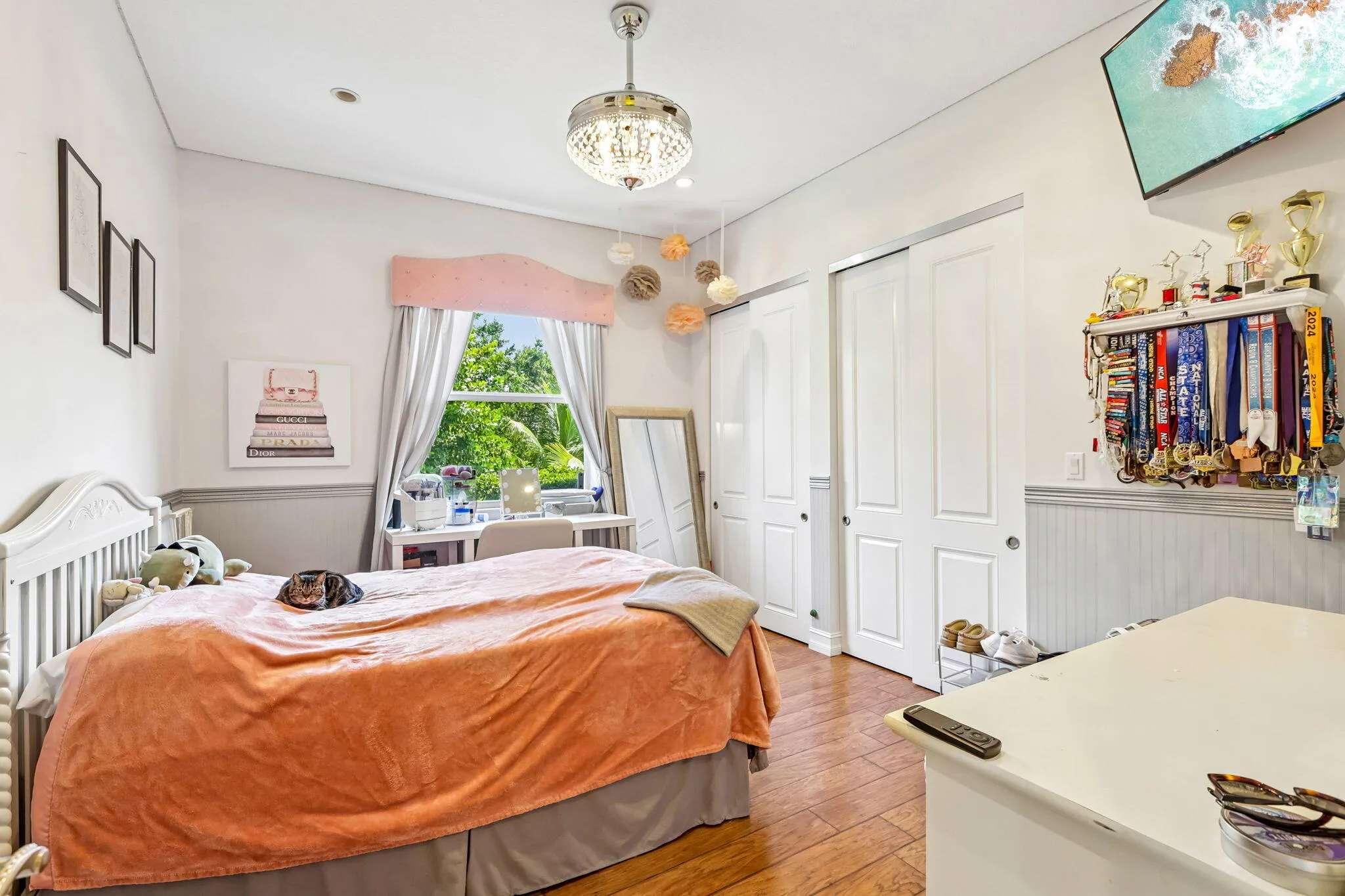 Bright room featuring wood-finish flooring, a large window with exterior tree views, and two white sliding closet doors