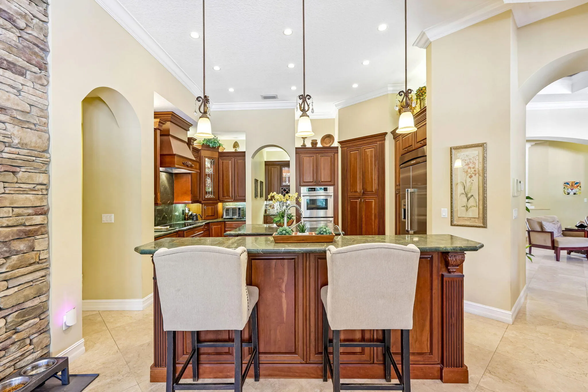 Gourmet kitchen featuring a large central island with seating, dark wood cabinetry, stainless steel appliances, recessed lighting, and green countertops