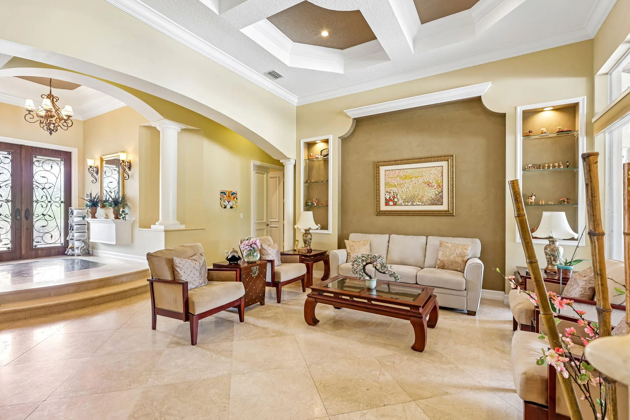 Spacious living area featuring coffered ceilings, large format tile flooring, and integrated display shelving with accent lighting