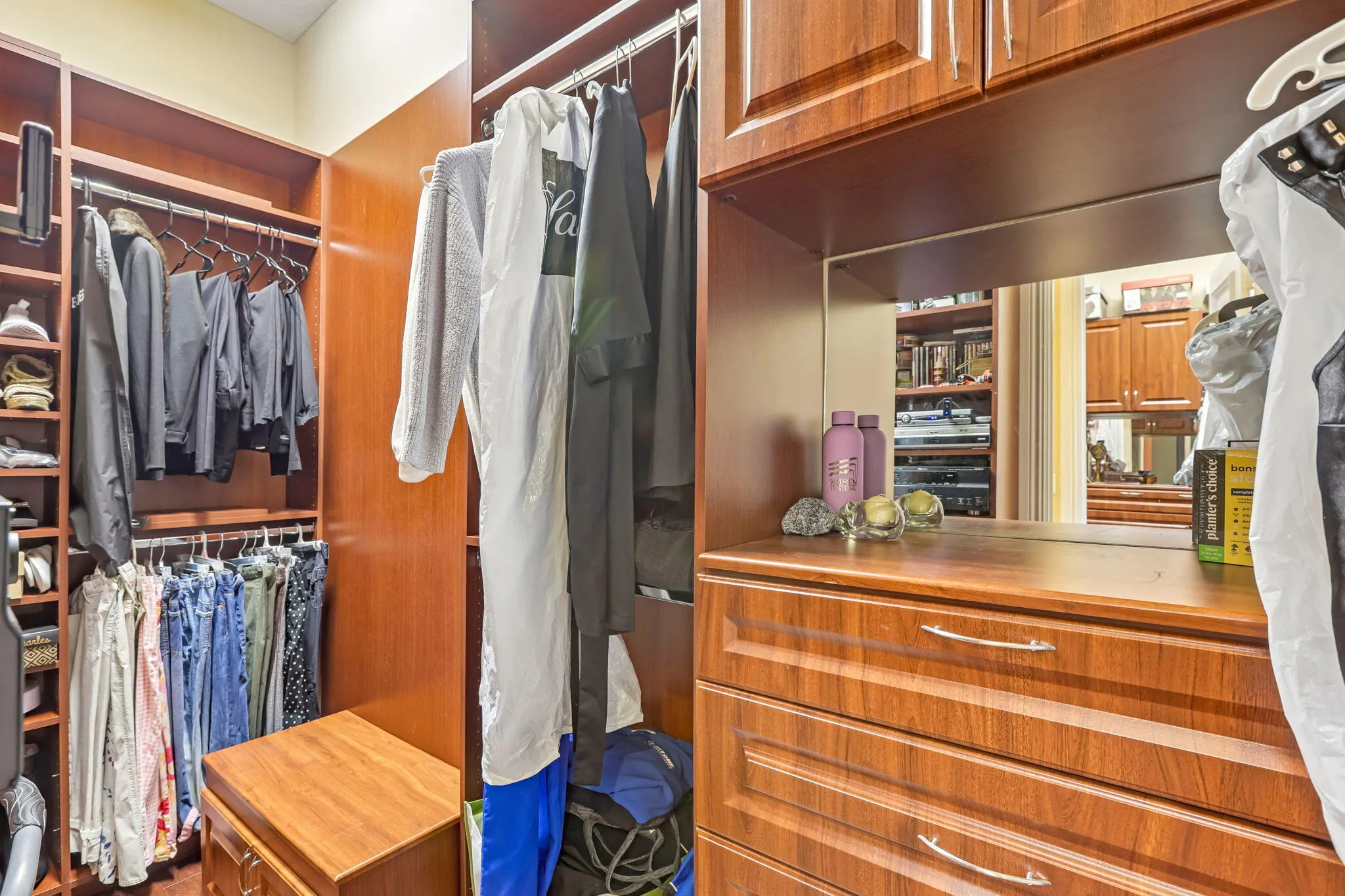 Expansive custom closet featuring warm wood-finish cabinetry, integrated shelving, multiple hanging rods, built-in drawers, and a recessed mirror