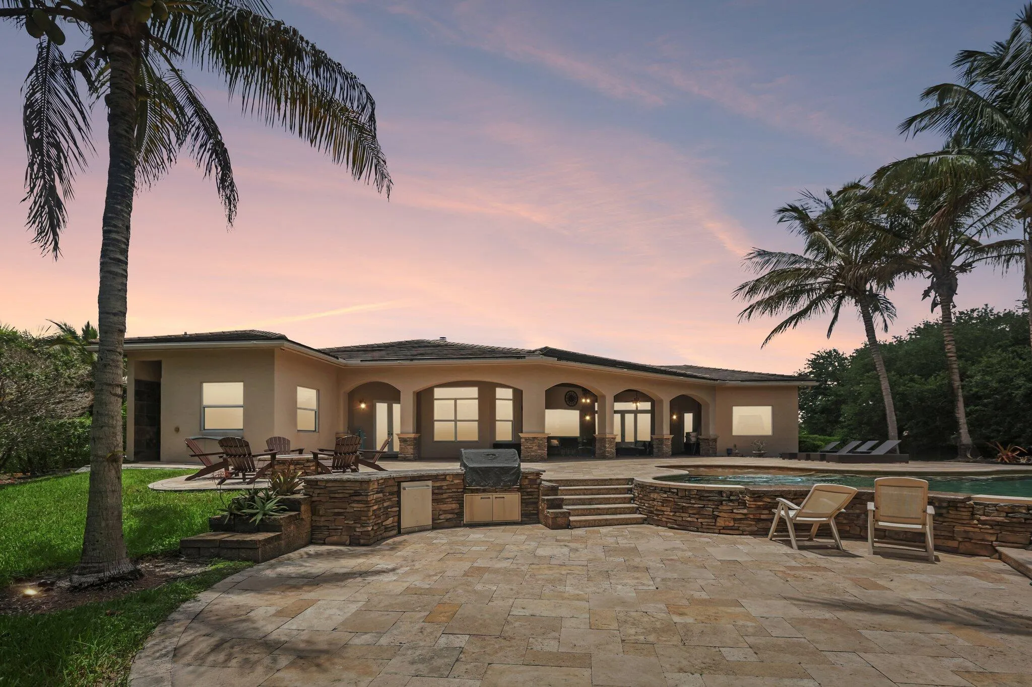 Outdoor living space featuring a stone-paver patio, built-in outdoor kitchen, and an integrated pool and spa
