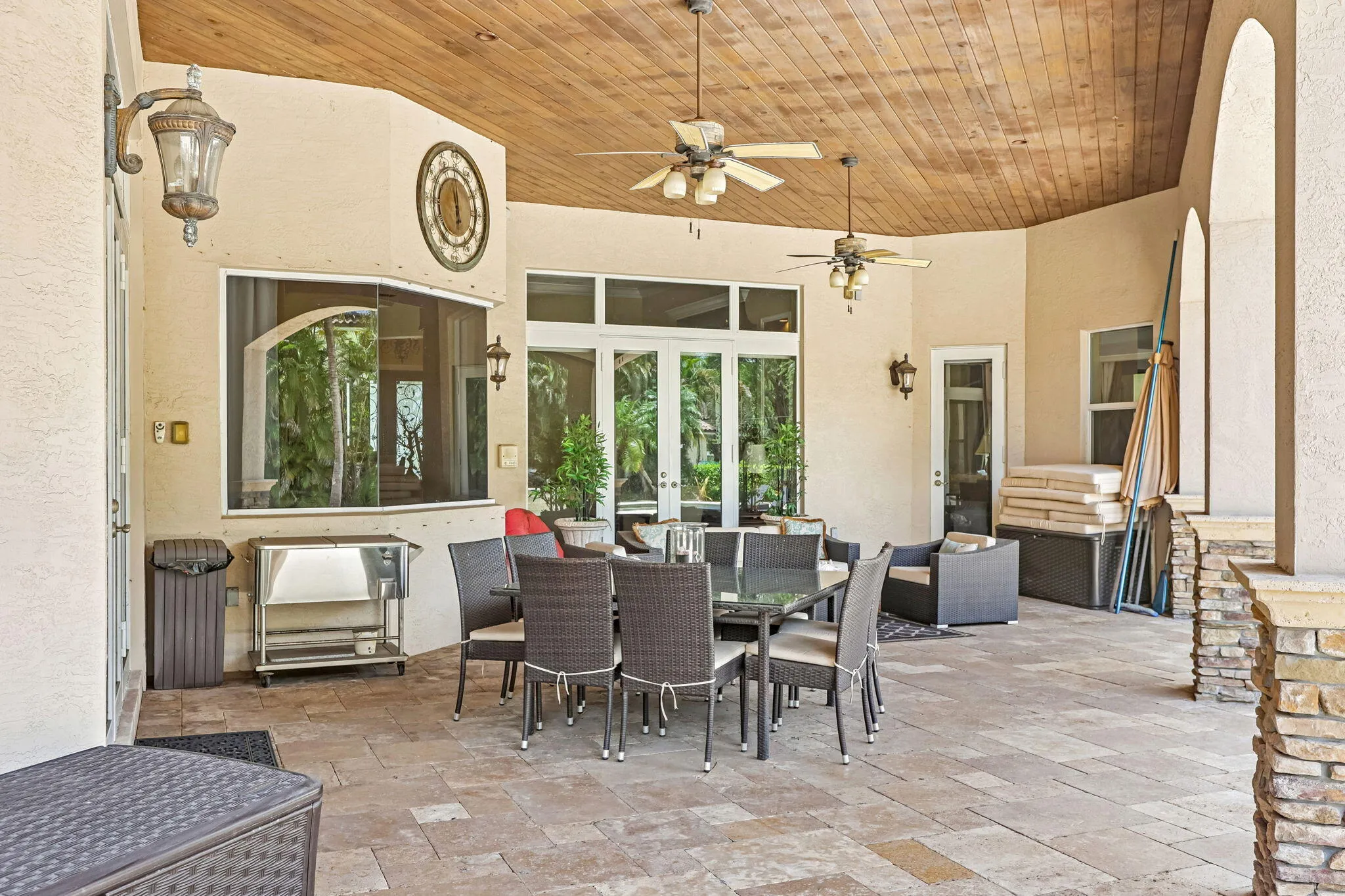 Expansive outdoor patio featuring a wood-finish ceiling, multiple ceiling fans, and sconce lighting