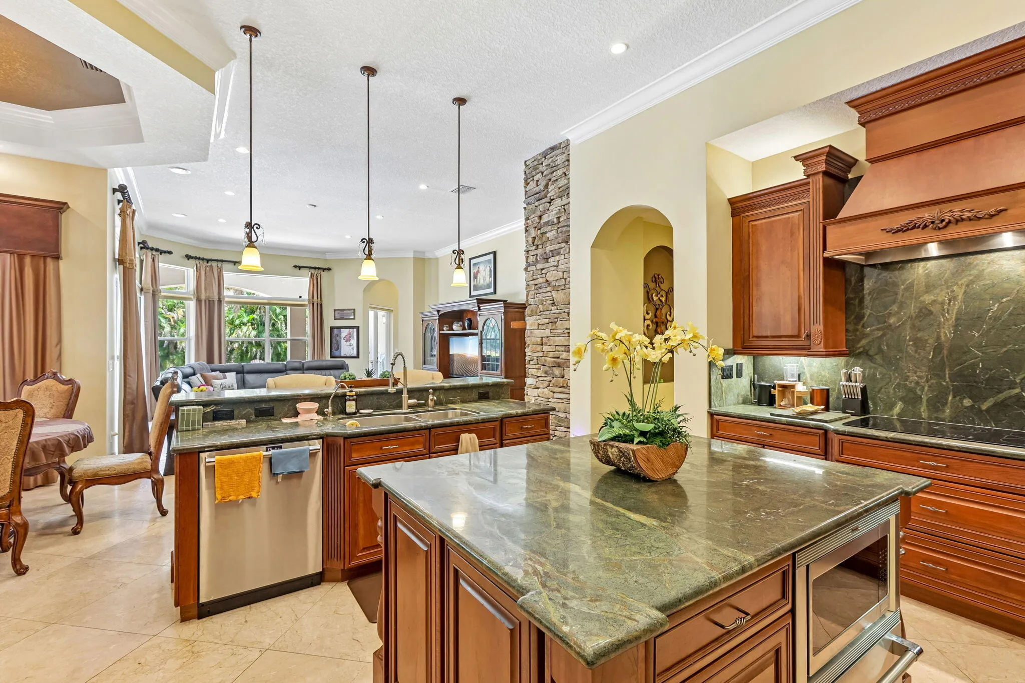 Kitchen featuring rich wood cabinetry, stone countertops, a central island with built-in microwave, stainless steel appliances, and pendant lighting