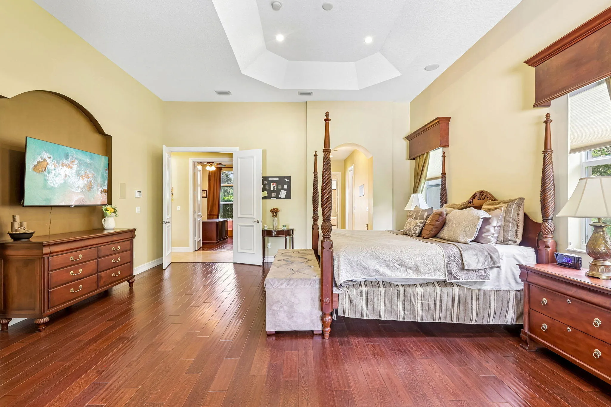 Spacious room featuring wood-finish flooring, a tray ceiling with recessed lighting, and double door entryways