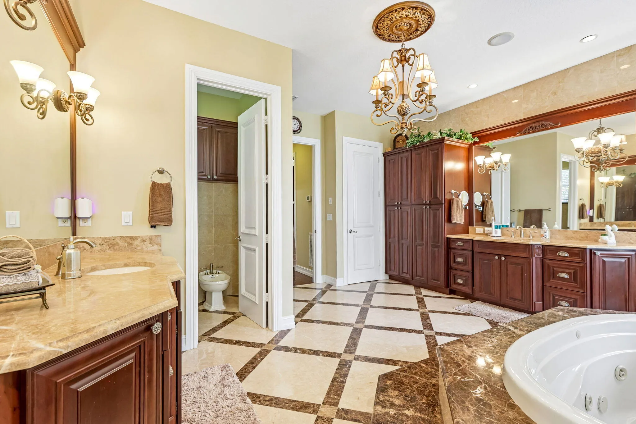 Expansive bathroom featuring a checkerboard tile floor, a recessed jetted tub with a stone surround, and dual vanity areas with stone countertops and wood cabinetry