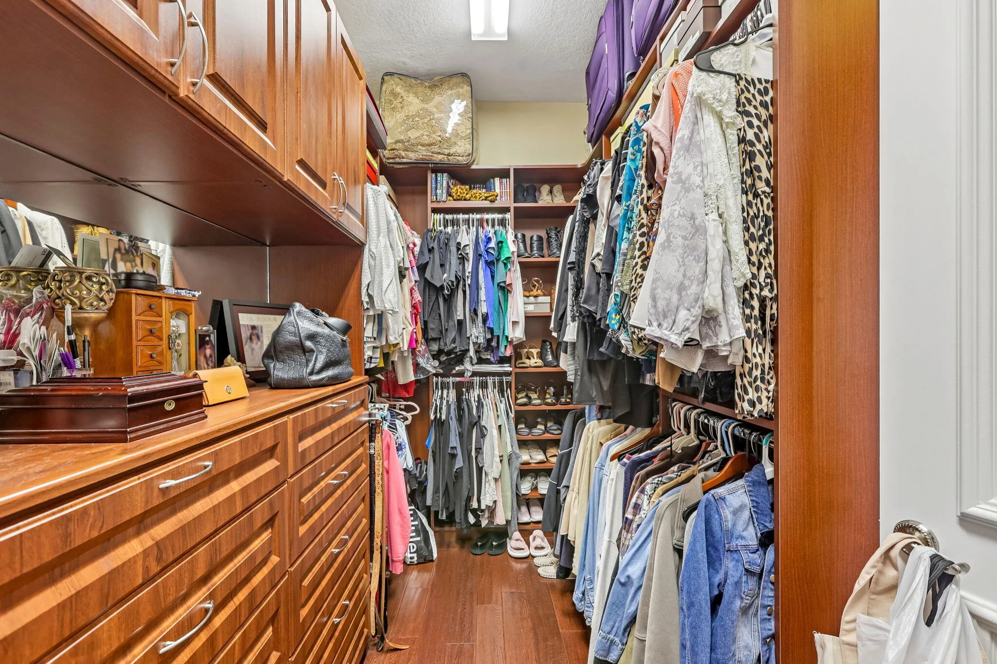 Custom-built closet featuring extensive wood cabinetry, multiple hanging rods, dedicated shoe shelving, and upper storage compartments