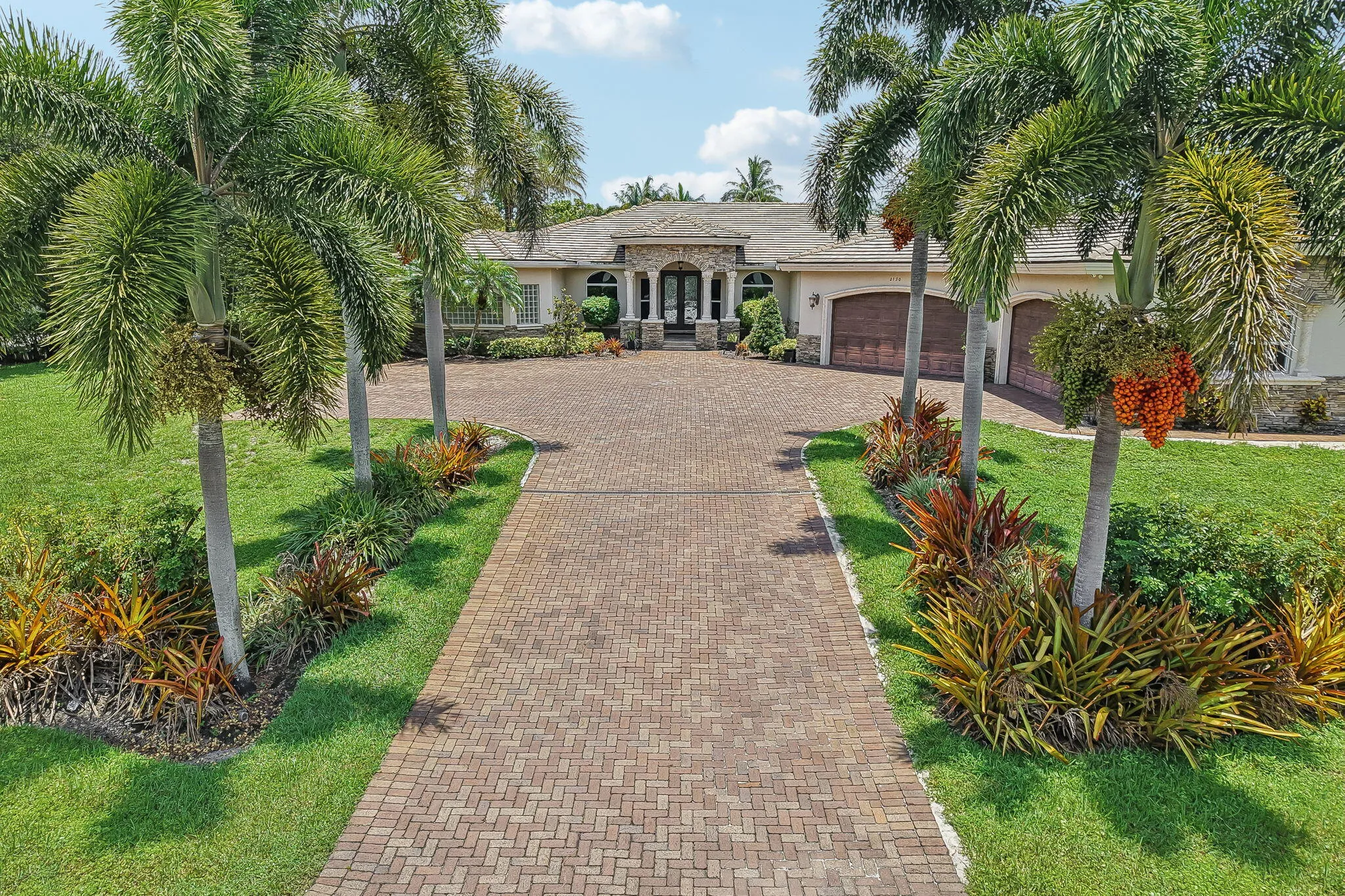 Paver driveway framed by lush tropical landscaping and mature palm trees