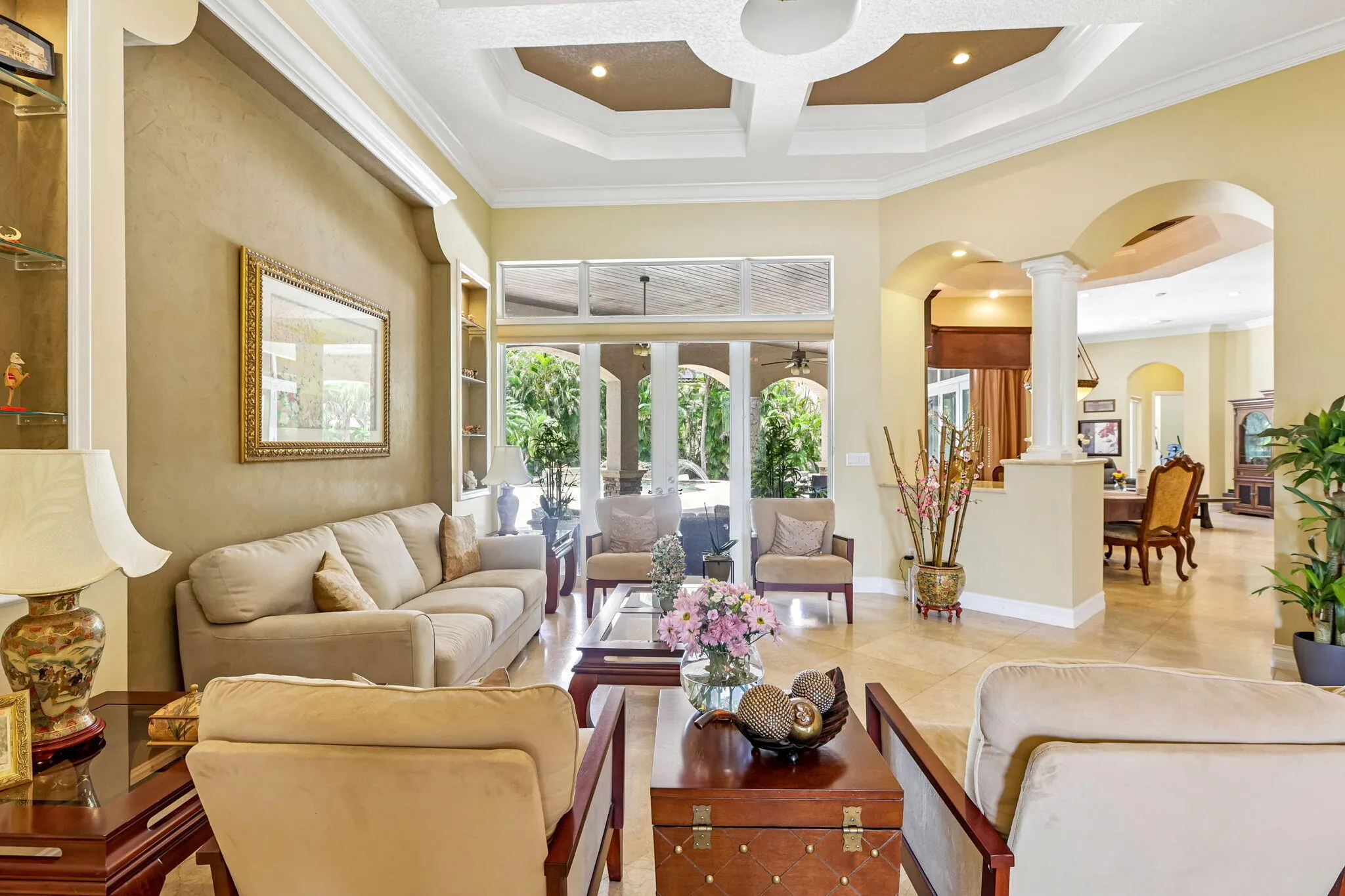 Spacious living area featuring coffered ceilings, built-in display shelving, and glass sliding doors