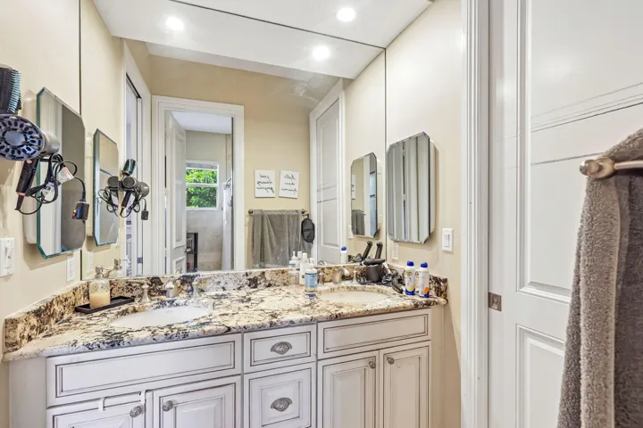 Dual vanity featuring a granite countertop with integrated sinks and white cabinetry