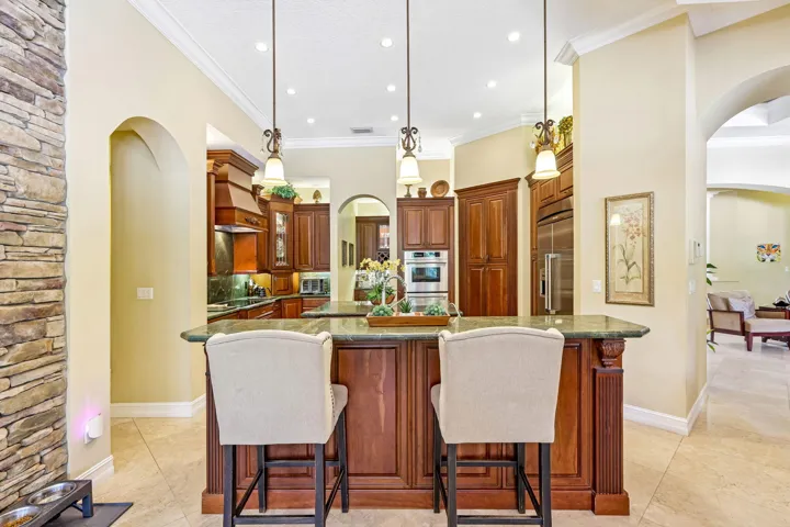 Gourmet kitchen featuring a large central island with seating, dark wood cabinetry, stainless steel appliances, recessed lighting, and green countertops