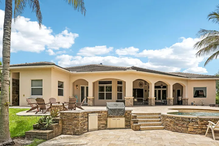 Expansive outdoor living area featuring a built-in outdoor kitchen, stone-clad spa, and stepped paver patio