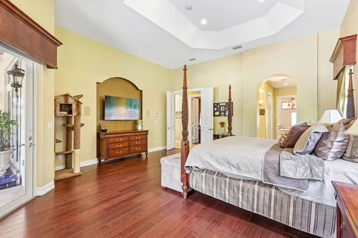 Spacious bedroom featuring wood-finish flooring, a tray ceiling with recessed lighting, an arched wall niche, and patio access through French doors