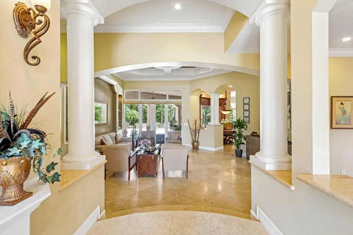 Spacious interior featuring a tiled entry, arched doorways, decorative columns, tray ceilings, and glass-paneled doors