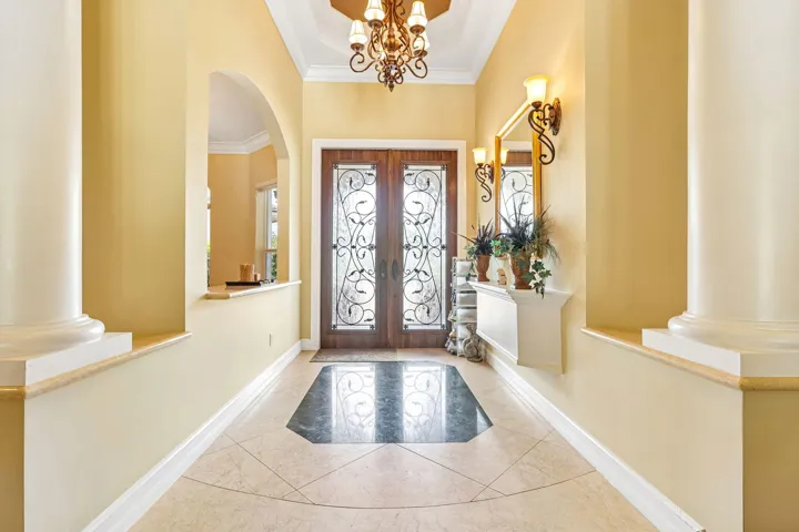 Entry foyer featuring double wooden doors with decorative glass inserts, a coffered ceiling with a chandelier, and sconce lighting