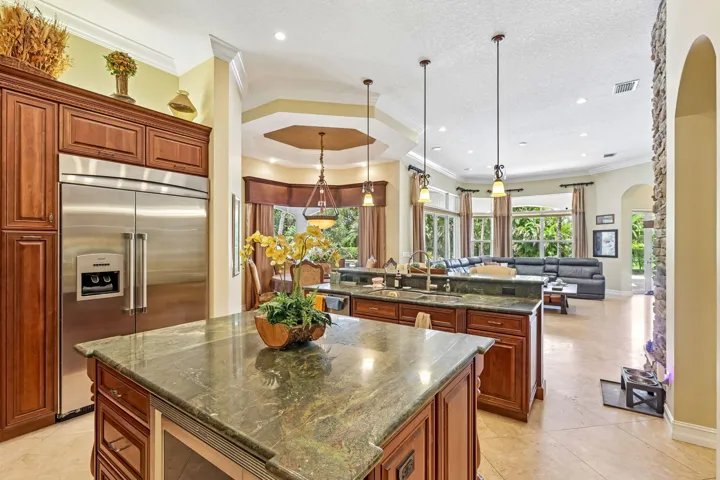 Gourmet kitchen featuring a large stainless steel refrigerator, dark wood cabinetry, an expansive kitchen island with a stone countertop, an integrated wine cooler, and pendant lighting