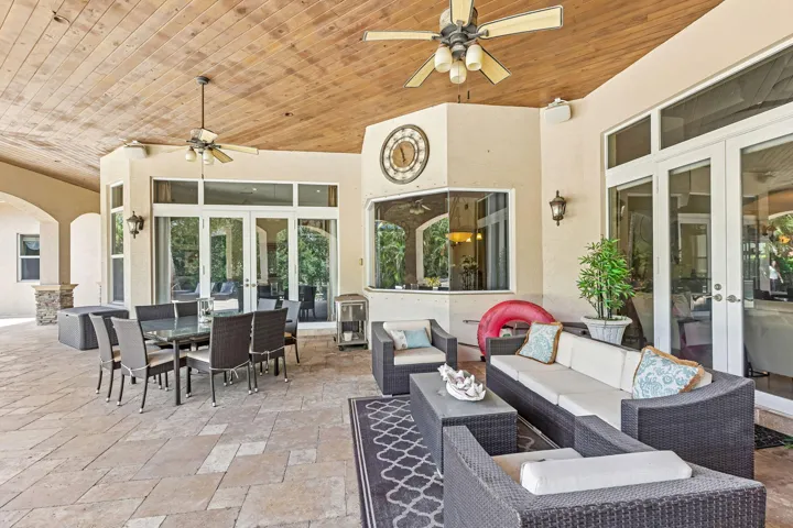 Covered outdoor living space featuring paver flooring, a wood-finish ceiling, multiple ceiling fans, large glass sliding doors, and a built-in outdoor bar