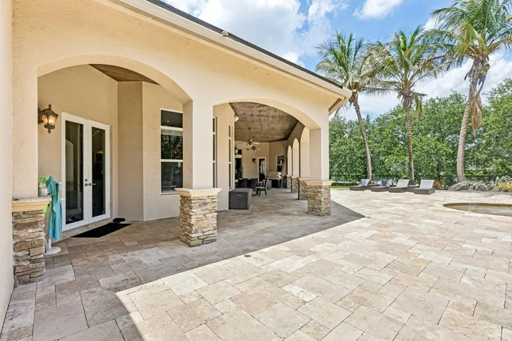 Expansive paver patio with a covered lanai, integrated spa, and mature palm trees