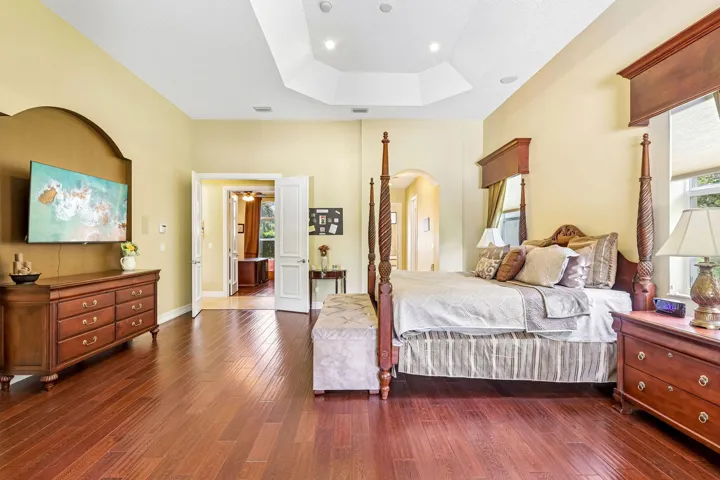 Spacious room featuring wood-finish flooring, a tray ceiling with recessed lighting, and double door entryways