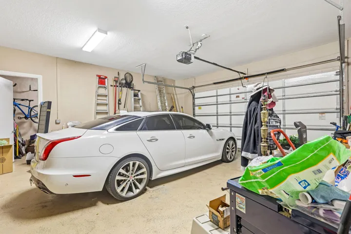 Attached garage featuring a white overhead door, textured ceiling, fluorescent lighting, and a painted concrete floor