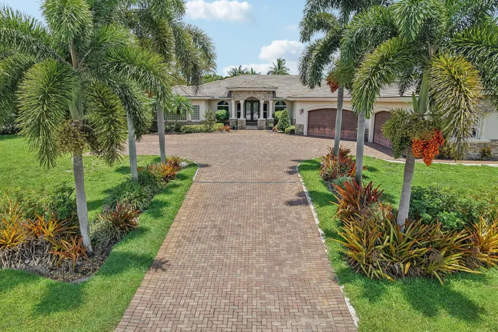 Paver driveway framed by lush tropical landscaping and mature palm trees