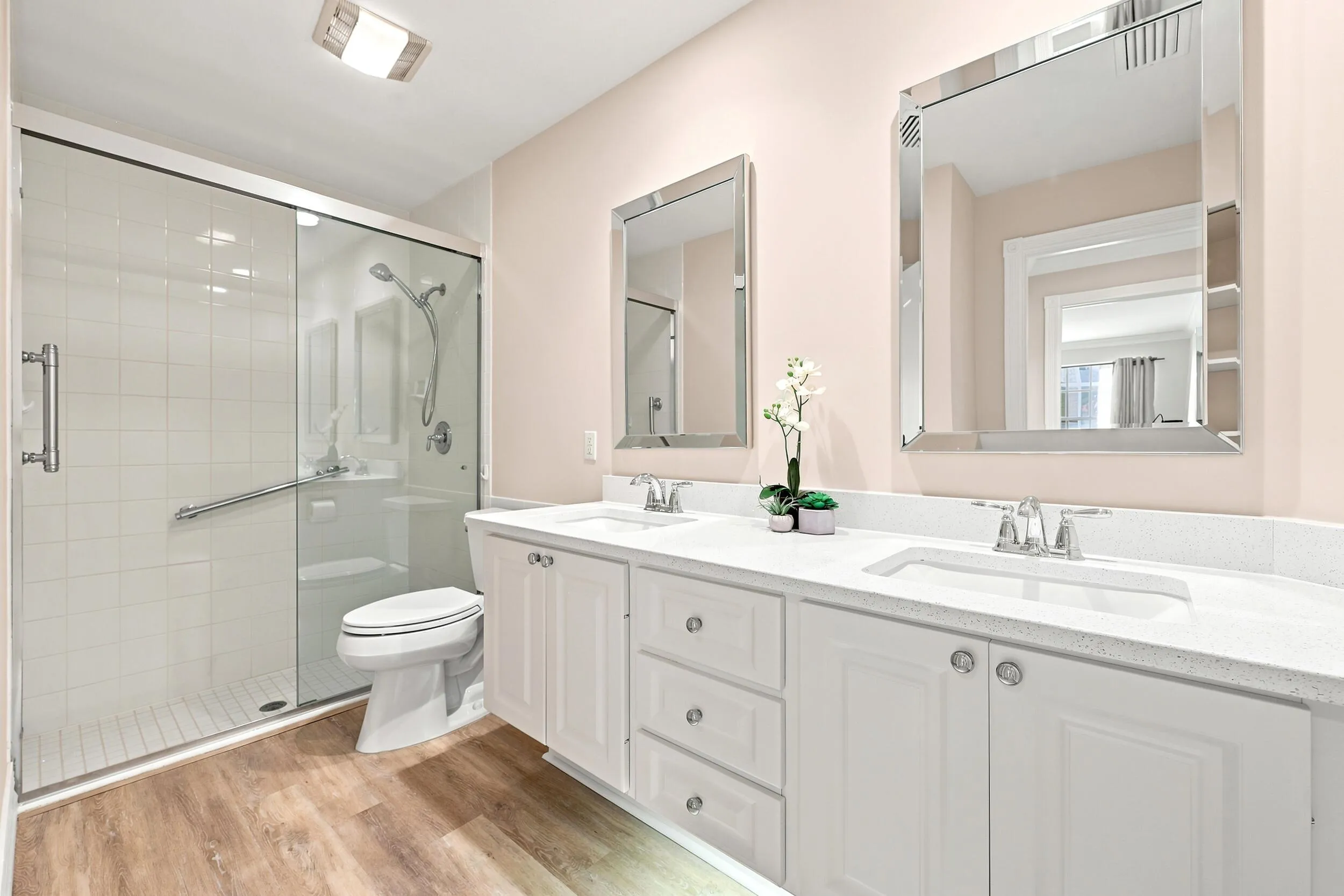 Dual vanity with undermount sinks and white shaker-style cabinetry, complemented by a glass-enclosed shower with white subway tile