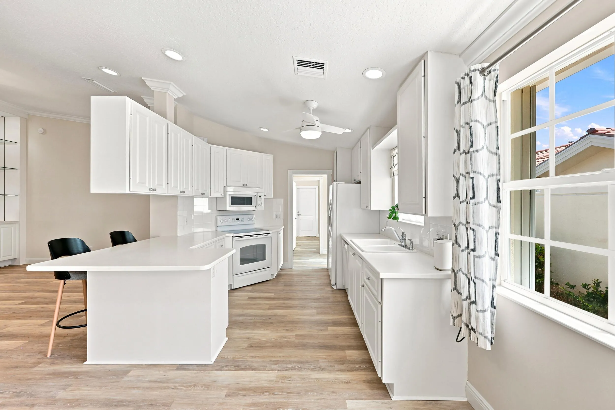 Kitchen featuring extensive white cabinetry, an integrated island with seating, wood-finish flooring, recessed lighting, and a window with grid patterns