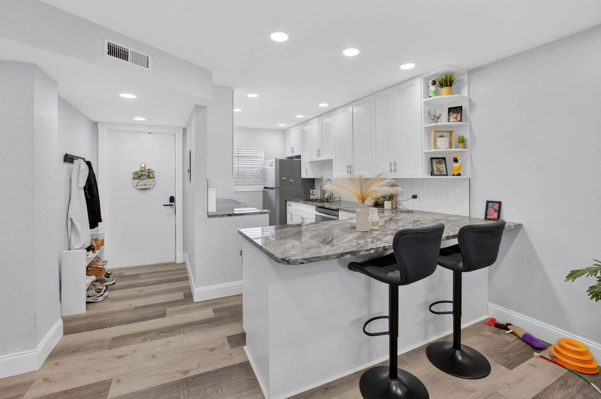 Open-concept kitchen featuring white cabinetry, gray stone-finish countertops, subway tile backsplash, and wood-finish flooring